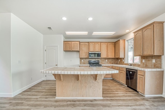 kitchen with a kitchen bar, tile countertops, a center island, stainless steel appliances, and light hardwood / wood-style flooring