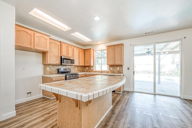 kitchen featuring backsplash, light wood-type flooring, stainless steel appliances, tile counters, and a center island