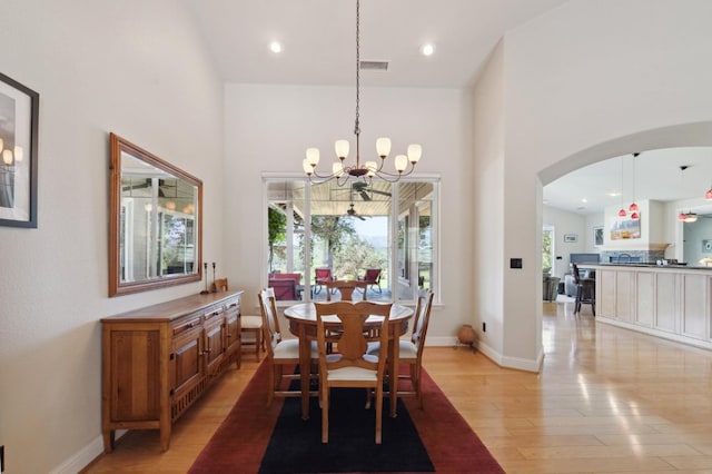 dining space with light hardwood / wood-style flooring, a high ceiling, and an inviting chandelier