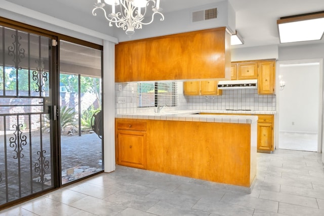 kitchen with an inviting chandelier, kitchen peninsula, tile counters, and tasteful backsplash