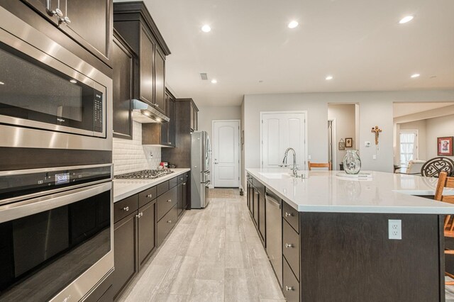 kitchen featuring a kitchen island with sink, a breakfast bar area, stainless steel appliances, sink, and light wood-type flooring