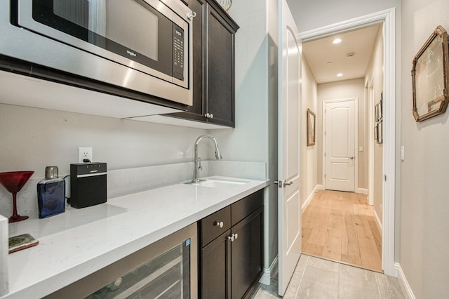 kitchen featuring wine cooler, dark brown cabinets, stainless steel microwave, light wood-type flooring, and sink