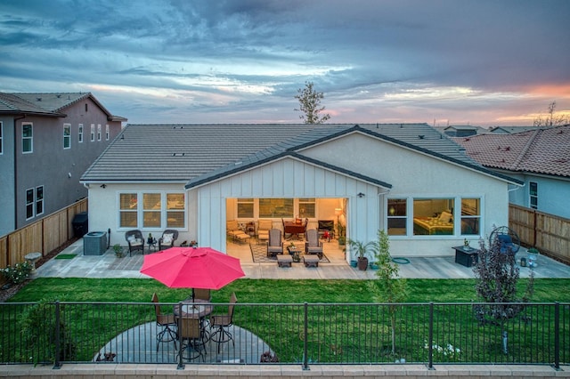 back house at dusk with a yard, a patio area, and central AC unit