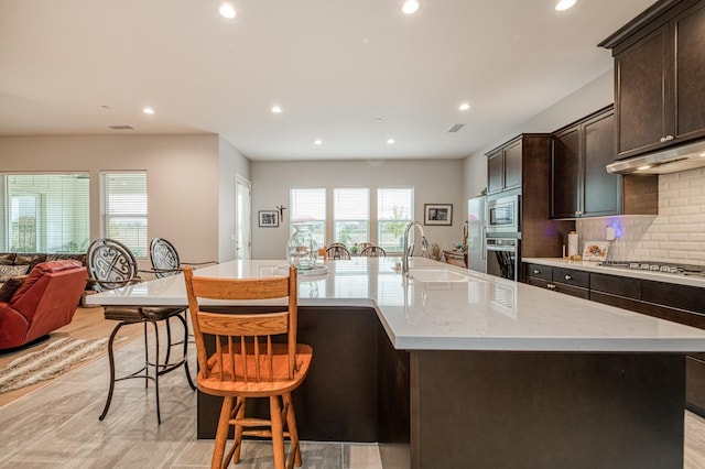 kitchen featuring a large island with sink, sink, light wood-type flooring, appliances with stainless steel finishes, and tasteful backsplash