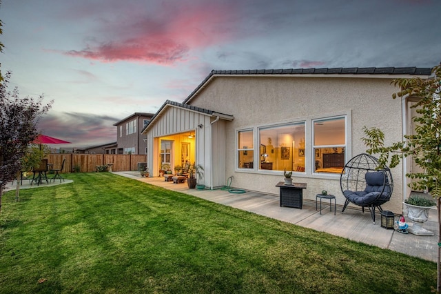 back house at dusk featuring a patio and a lawn