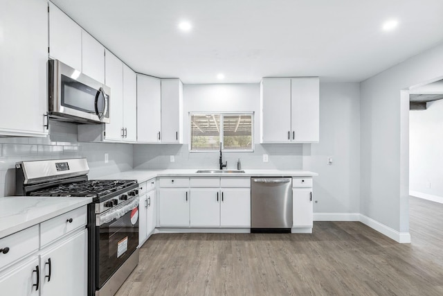 kitchen with light hardwood / wood-style floors, light stone counters, white cabinets, stainless steel appliances, and sink