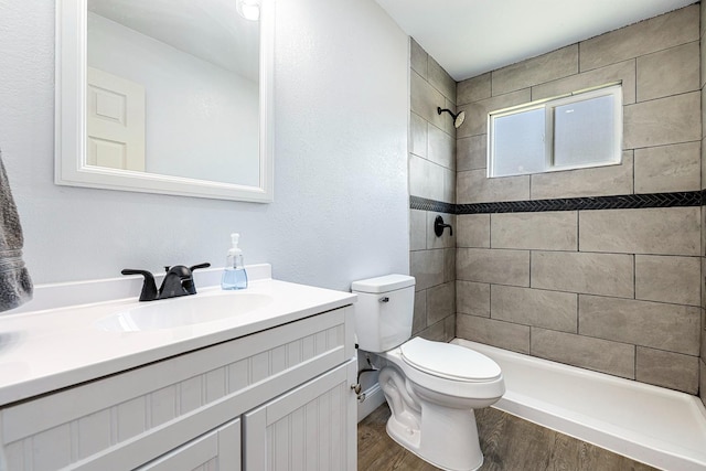 bathroom featuring a tile shower, wood-type flooring, vanity, and toilet