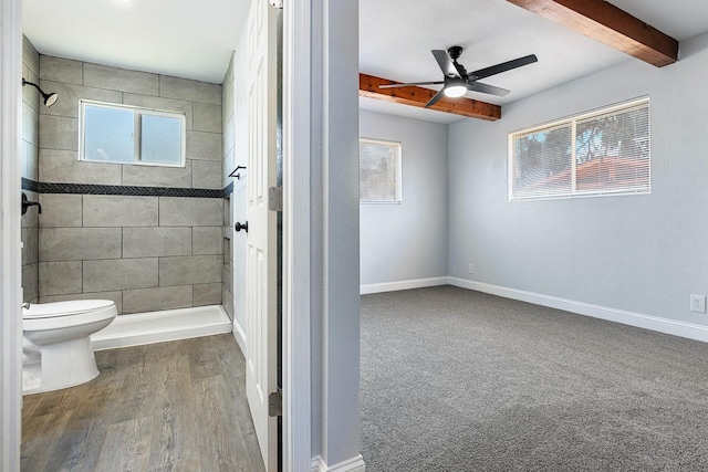 bathroom with ceiling fan, beamed ceiling, toilet, a tile shower, and hardwood / wood-style floors