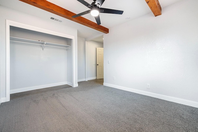 unfurnished bedroom with ceiling fan, beamed ceiling, a closet, and dark carpet