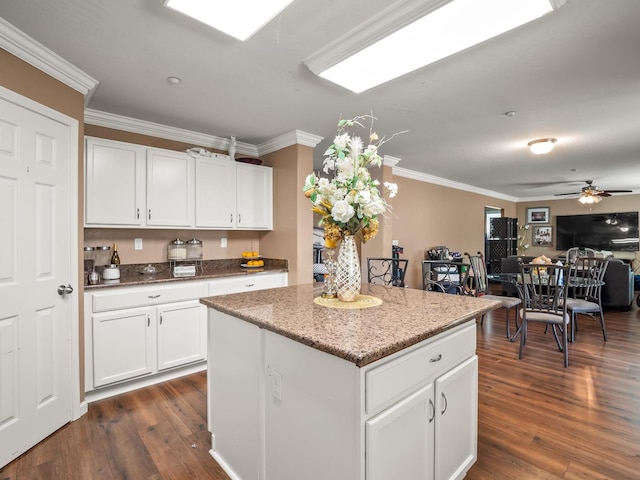 kitchen featuring dark wood-type flooring, white cabinetry, a kitchen island, crown molding, and ceiling fan