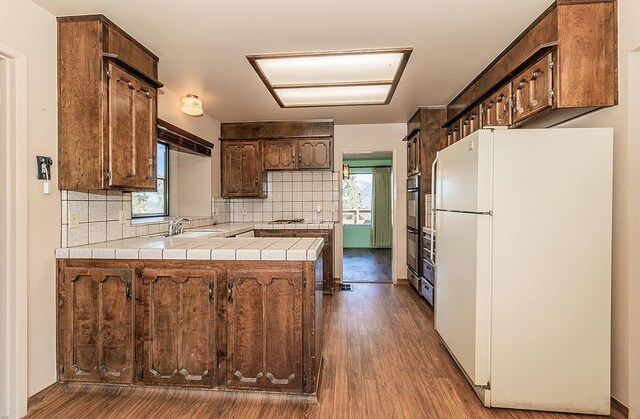 kitchen featuring white refrigerator, tile countertops, dark hardwood / wood-style flooring, and decorative backsplash