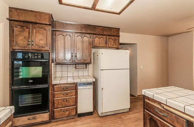 kitchen with light wood-type flooring, white refrigerator, backsplash, tile countertops, and black double oven