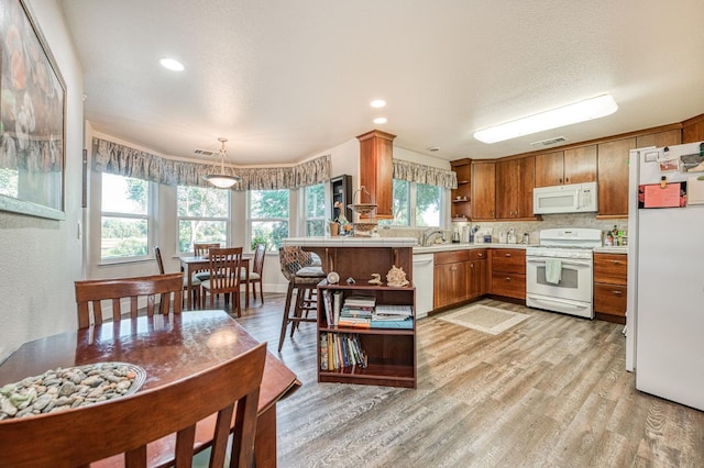 kitchen with light hardwood / wood-style floors, backsplash, white appliances, kitchen peninsula, and decorative light fixtures