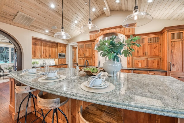 kitchen featuring pendant lighting, dark hardwood / wood-style floors, stainless steel microwave, vaulted ceiling with beams, and stone countertops