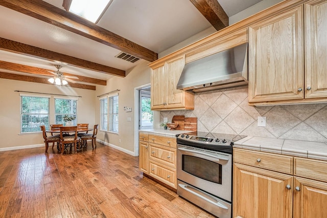 kitchen featuring ceiling fan, beam ceiling, wall chimney range hood, electric stove, and light hardwood / wood-style floors