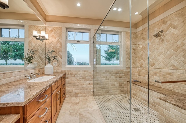 bathroom with a healthy amount of sunlight, tile walls, walk in shower, and vanity