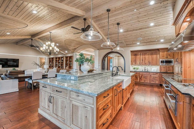 kitchen with a large island with sink, ceiling fan with notable chandelier, stainless steel microwave, dark hardwood / wood-style floors, and sink