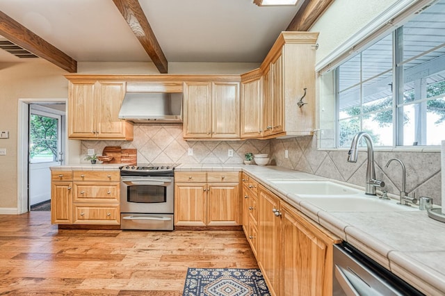 kitchen featuring a wealth of natural light, range hood, beam ceiling, stainless steel appliances, and tile countertops