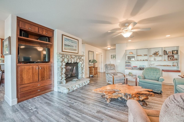 living room featuring ceiling fan, a stone fireplace, and wood-type flooring