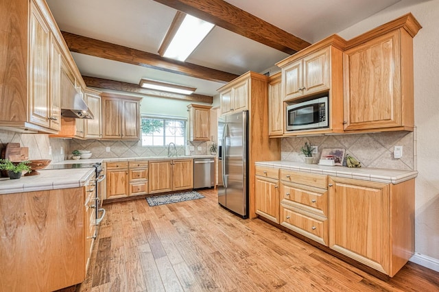 kitchen featuring stainless steel appliances, light hardwood / wood-style floors, beamed ceiling, and tile countertops