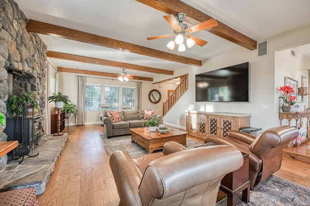 living room featuring ceiling fan, beamed ceiling, a fireplace, and light hardwood / wood-style flooring