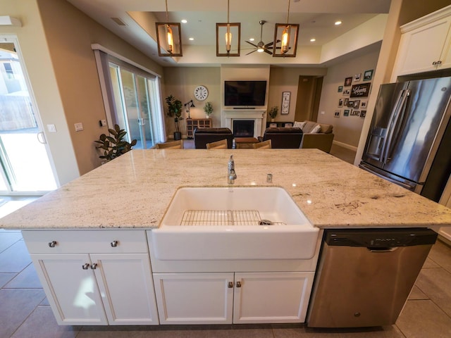 kitchen with appliances with stainless steel finishes, white cabinets, hanging light fixtures, light stone countertops, and a center island with sink