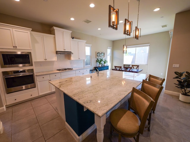 kitchen featuring white cabinetry, appliances with stainless steel finishes, decorative light fixtures, and a kitchen island with sink