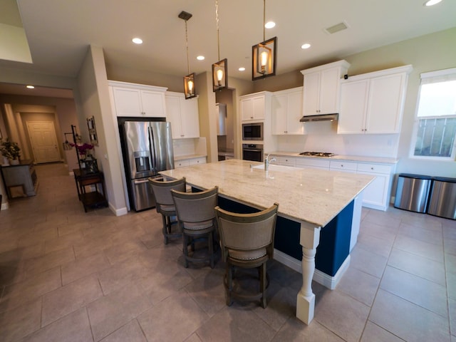 kitchen featuring decorative light fixtures, a center island with sink, stainless steel appliances, light stone countertops, and white cabinets