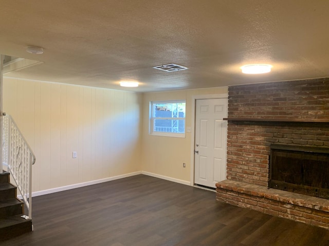 unfurnished living room featuring a textured ceiling, dark hardwood / wood-style flooring, and a brick fireplace