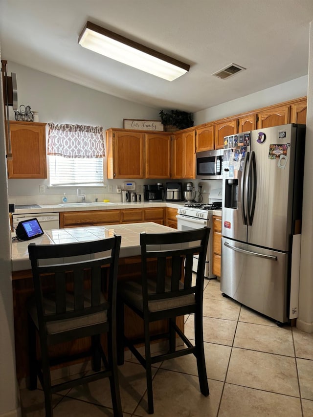 kitchen with tile counters, lofted ceiling, a kitchen bar, appliances with stainless steel finishes, and light tile patterned floors