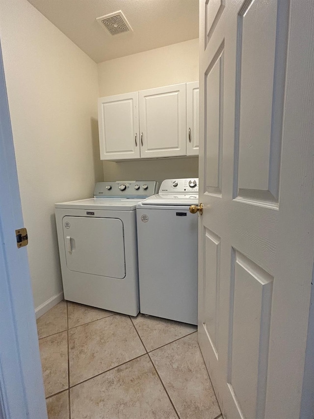 laundry room with light tile patterned flooring, washing machine and clothes dryer, and cabinets