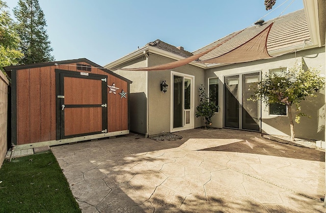 back of house featuring an outbuilding, a tile roof, stucco siding, a storage unit, and a patio area