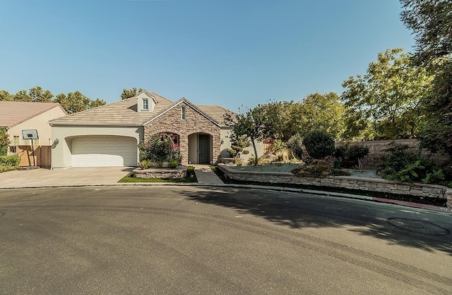 view of front of home with stucco siding, fence, a garage, stone siding, and driveway