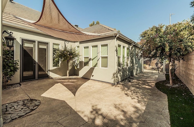 rear view of house with a tile roof, a patio area, fence, and stucco siding