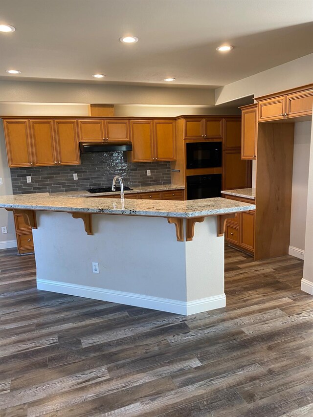 4707 N Arrow Ridge Way N, Clovis, CA 93619 - kitchen featuring under cabinet range hood, black appliances, brown cabinetry, a breakfast bar area, and recessed lighting