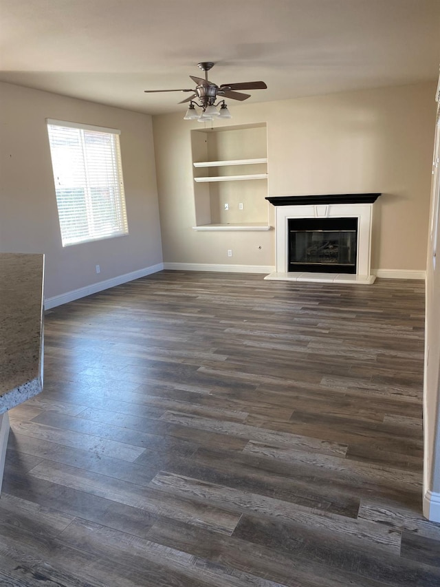 4707 N Arrow Ridge Way N, Clovis, CA 93619 - unfurnished living room featuring ceiling fan, baseboards, a glass covered fireplace, dark wood-style flooring, and built in features