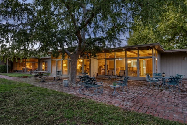 back house at dusk featuring a yard and a patio