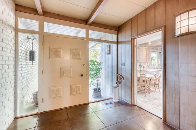 doorway featuring beam ceiling, tile patterned flooring, and wooden walls