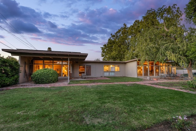 back house at dusk featuring a patio and a yard