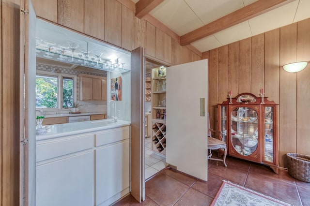 kitchen with tile patterned flooring, beamed ceiling, wooden walls, light brown cabinetry, and sink