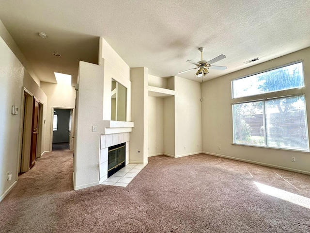 unfurnished living room with light carpet, ceiling fan, a tile fireplace, and a textured ceiling