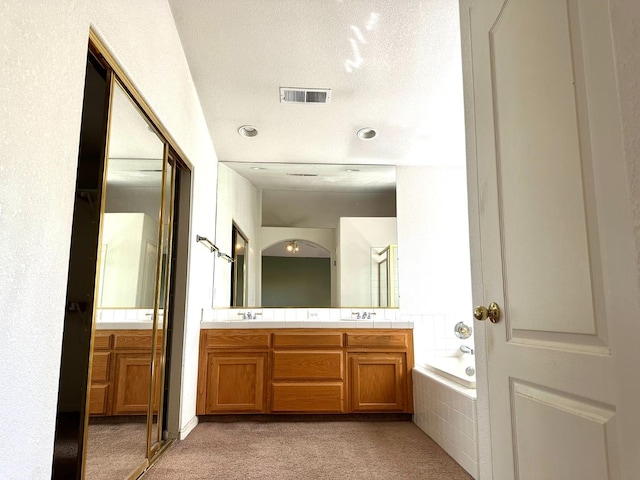 bathroom with vanity, tiled bath, and a textured ceiling