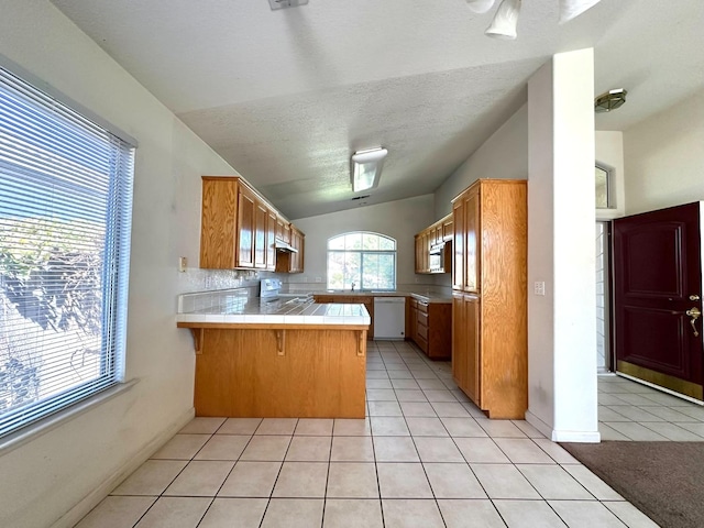 kitchen featuring tile counters, vaulted ceiling, kitchen peninsula, a kitchen breakfast bar, and white appliances