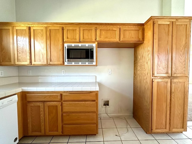 kitchen featuring dishwasher, tile countertops, stainless steel microwave, and light tile patterned floors