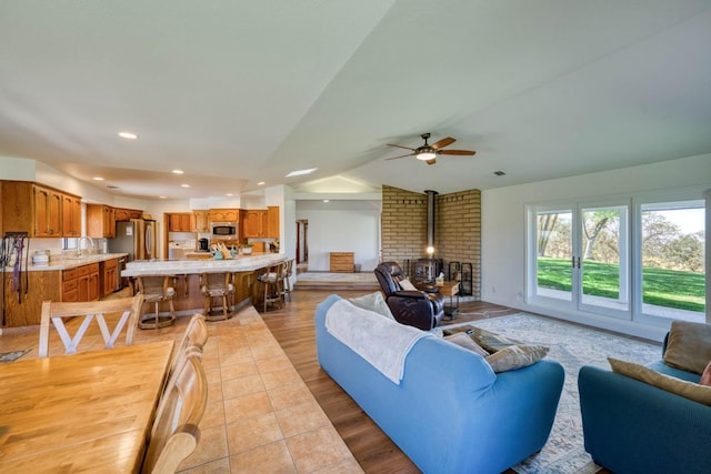 living room with sink, a wood stove, vaulted ceiling, light tile patterned floors, and ceiling fan