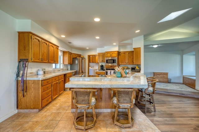 kitchen with light hardwood / wood-style floors, kitchen peninsula, a breakfast bar area, stainless steel appliances, and sink