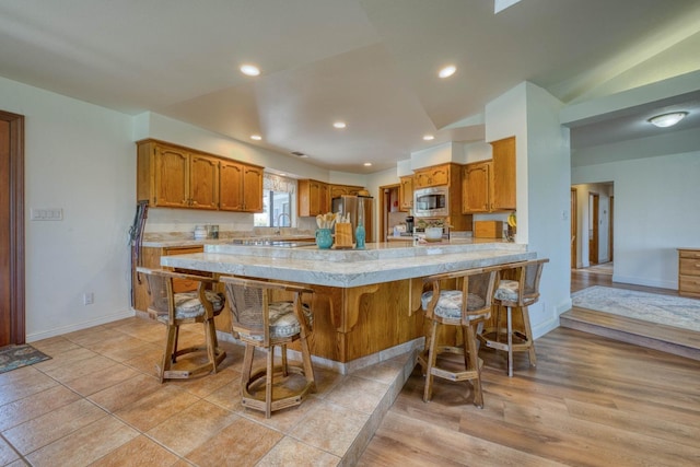 kitchen featuring a breakfast bar, lofted ceiling, kitchen peninsula, light hardwood / wood-style flooring, and stainless steel appliances