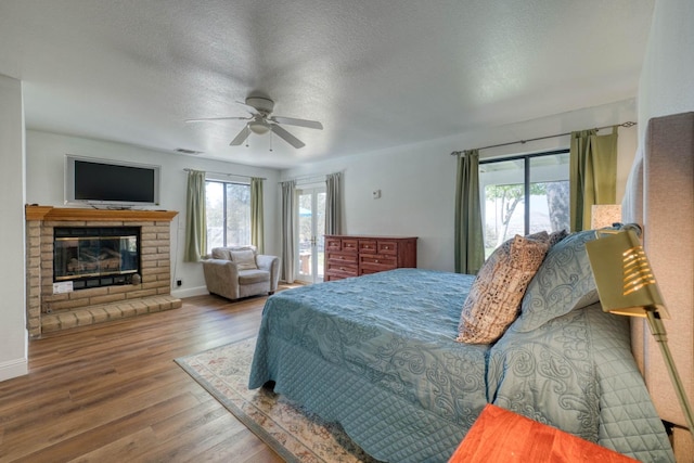 bedroom featuring multiple windows, wood-type flooring, a fireplace, and ceiling fan