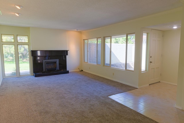 unfurnished living room with a textured ceiling, carpet floors, a tiled fireplace, and a wealth of natural light