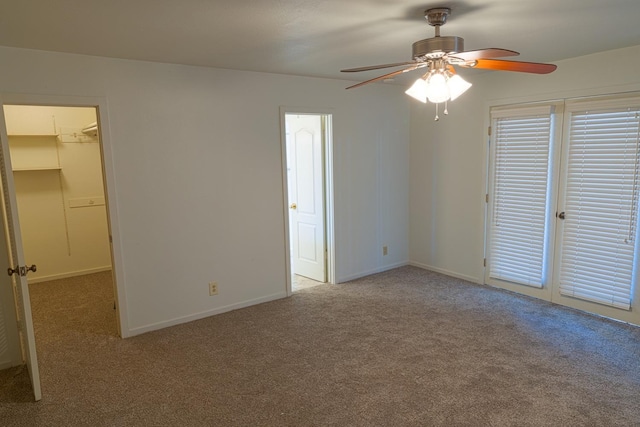 unfurnished bedroom with carpet, a spacious closet, baseboards, and ceiling fan